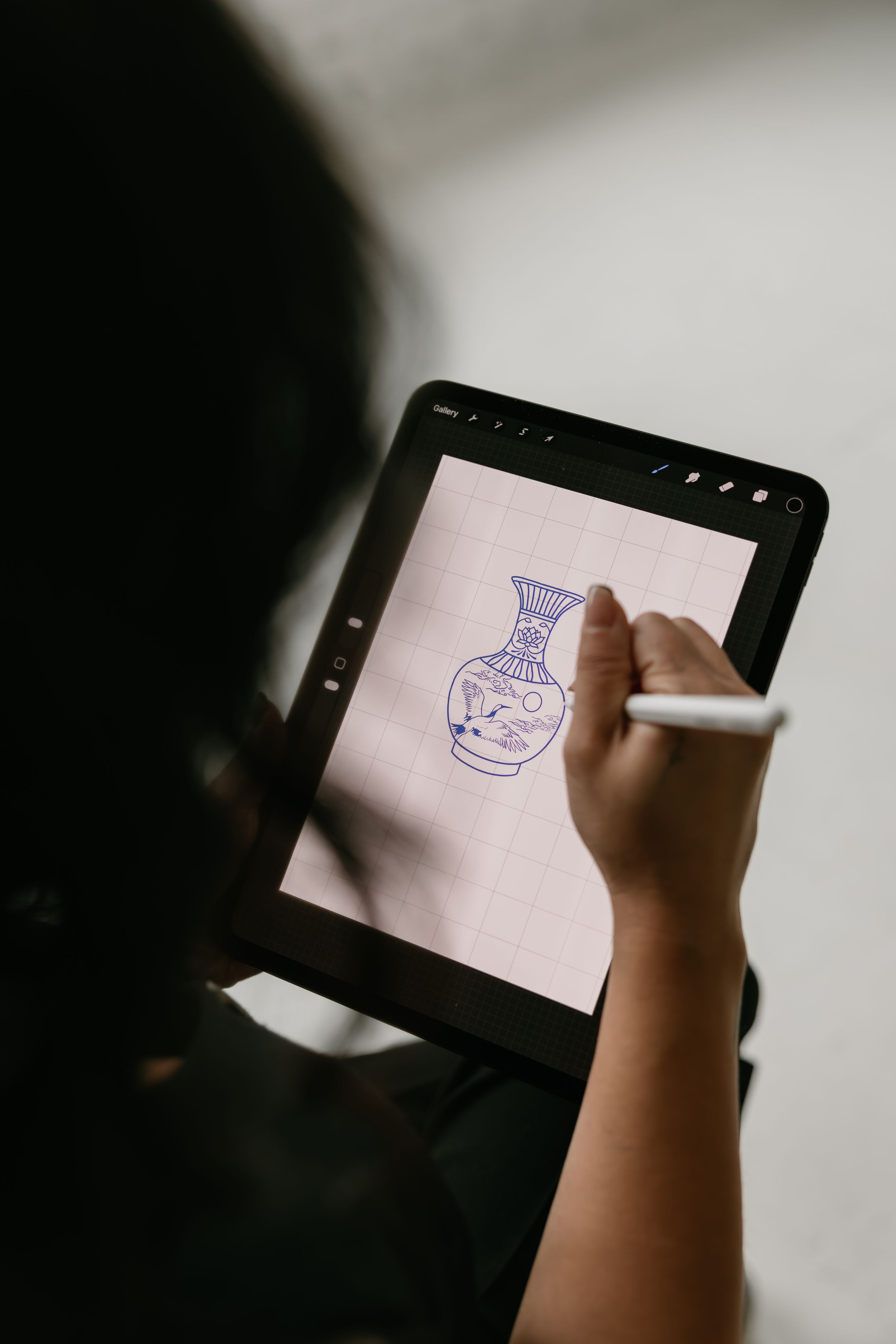 A person draws a decorative vase illustration on a digital tablet screen using a stylus pen.