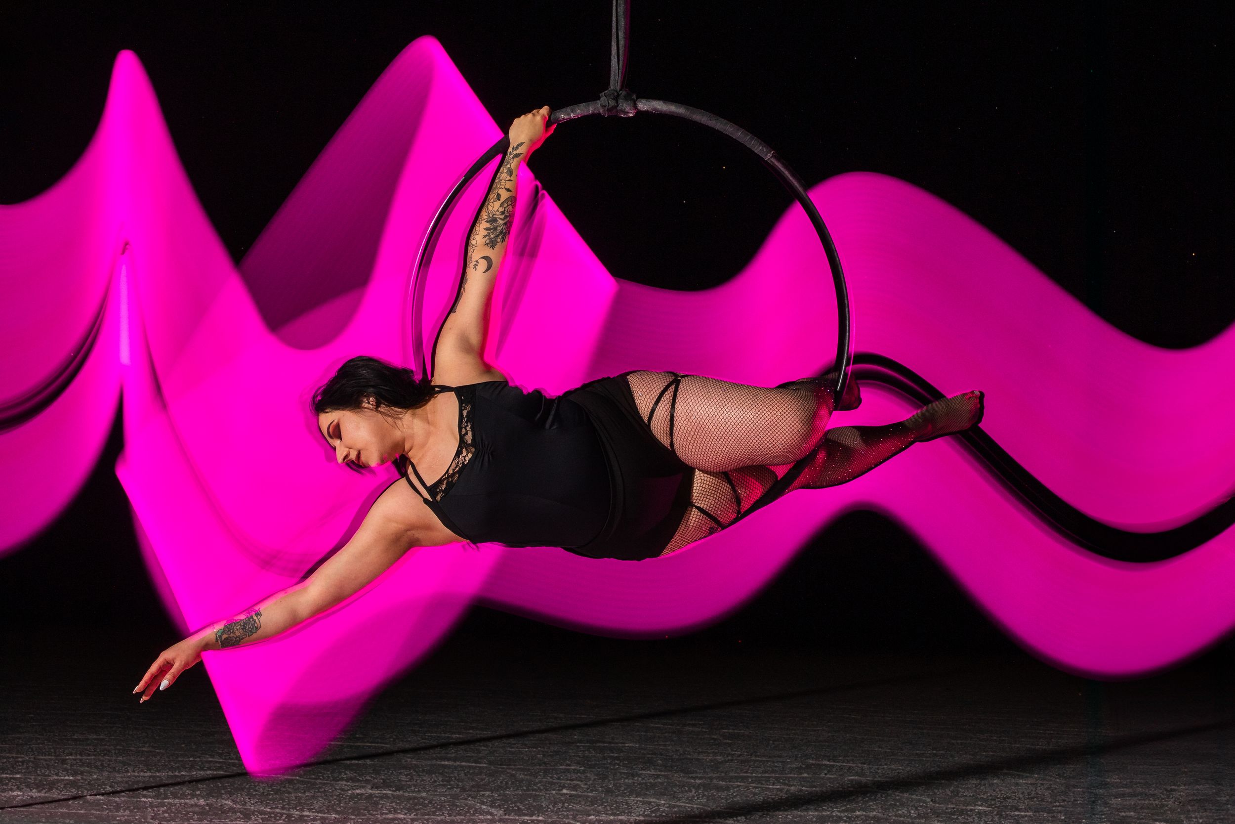Pink, aerialist mid-pose with swirling light painting; striking aerial arts portrait using long-exposure aerial photography.