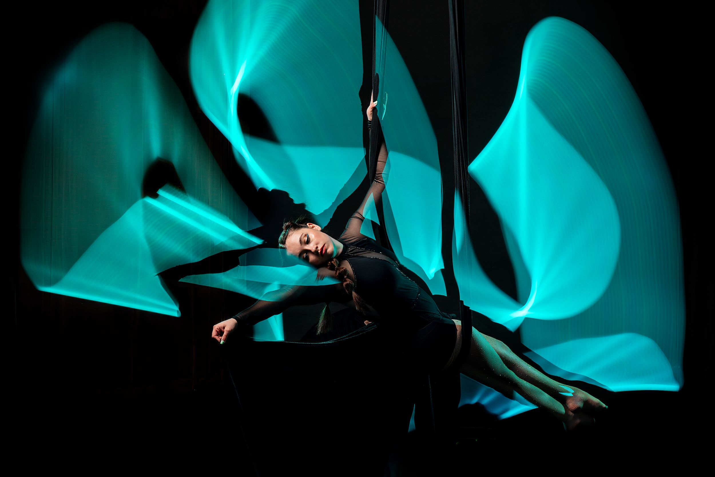 Cyan, Aerialist silhouette outlined by bright light painting; polished aerial arts photo capturing motion, color, and clean lines.