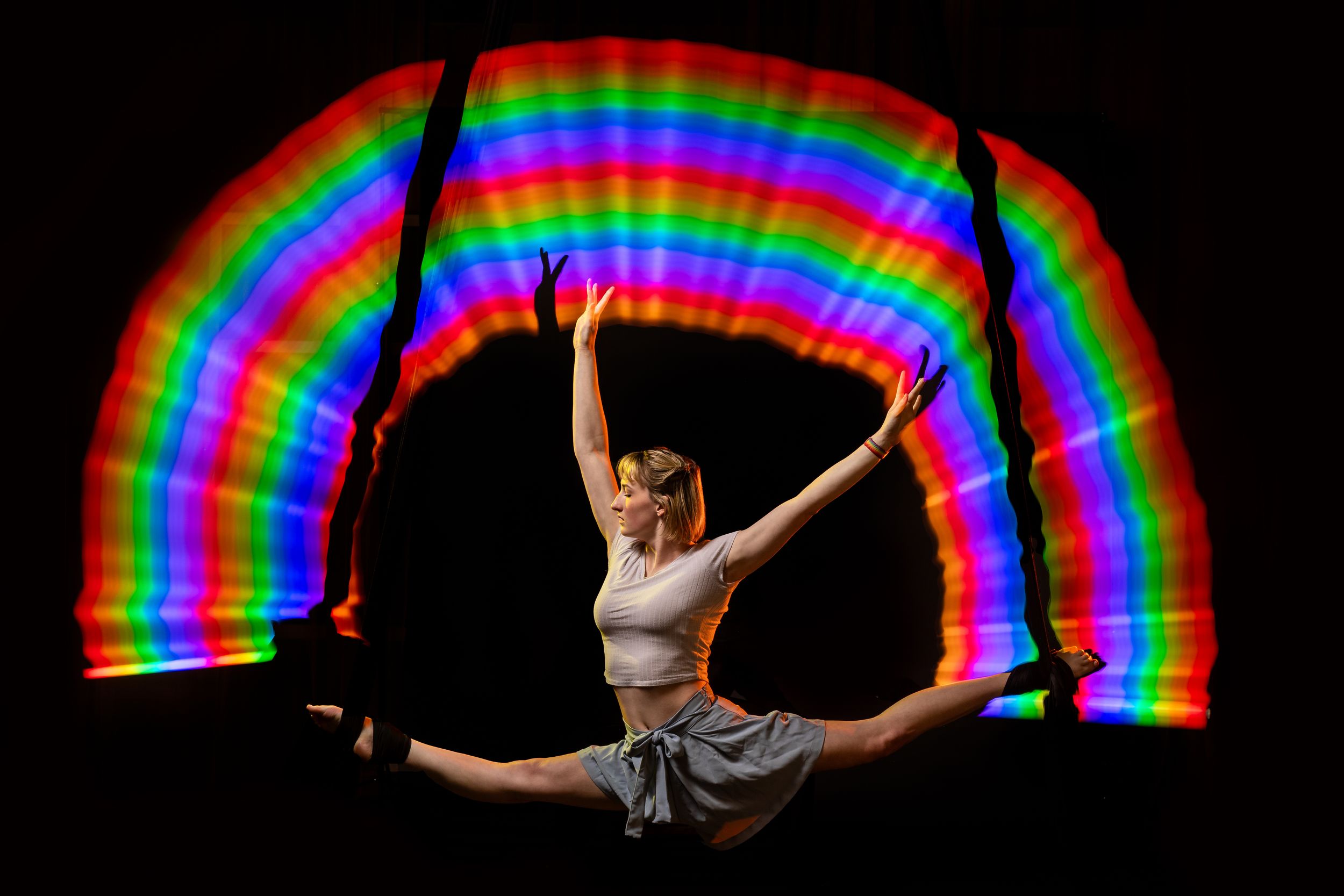 Rainbow Block, Aerialist silhouette outlined by bright light painting; polished aerial arts photo capturing motion, color, and clean lines.