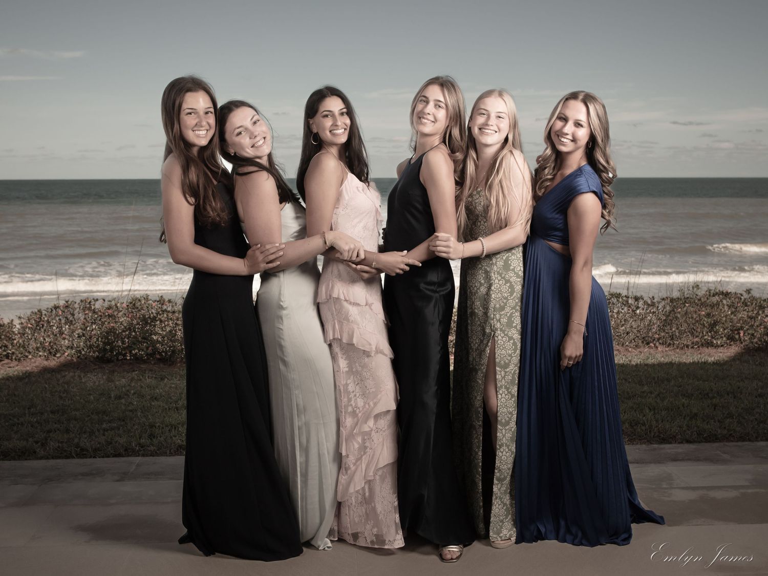 A group of women in formal dresses pose together at Ponte Vedra beach during sunset.