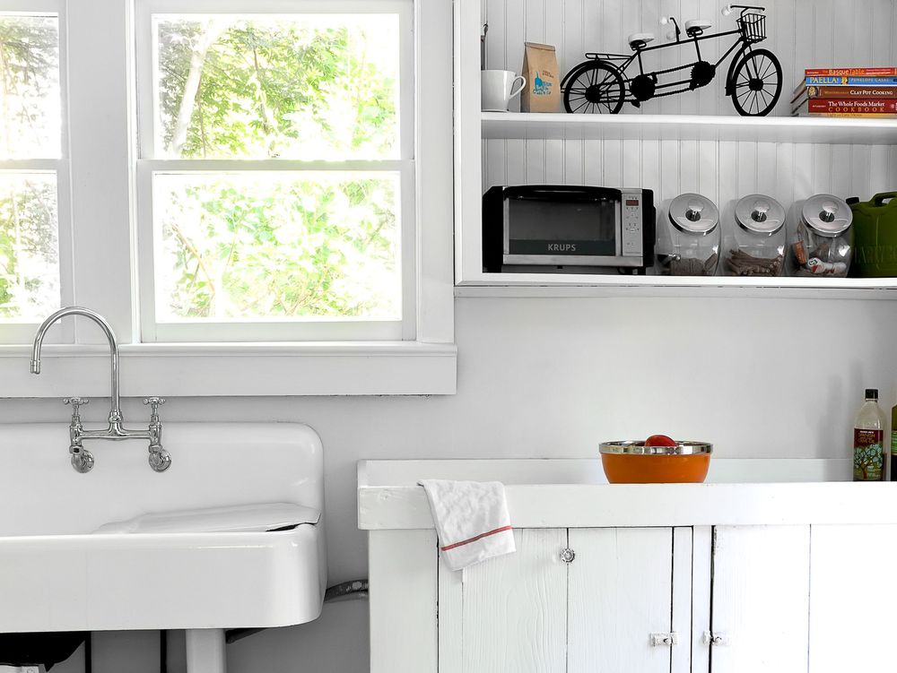 White farmhouse kitchen with vintage sink, window, and decorative bicycle model displayed on floating shelf.