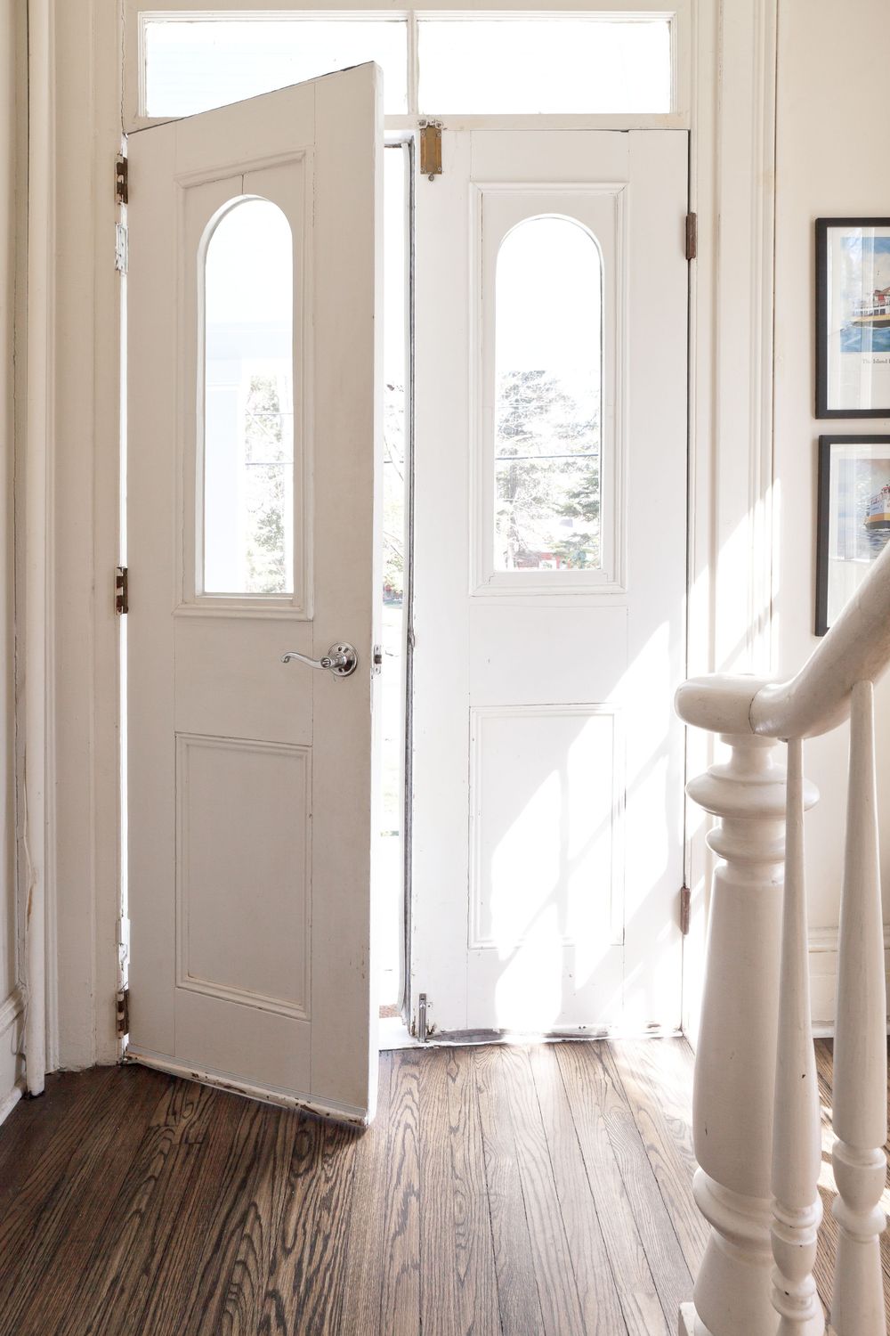 Bright white hallway with hardwood floors and natural light streaming through multiple windows and doors.