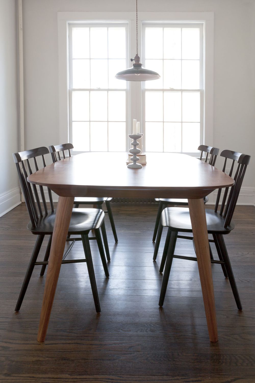 Minimalist dining area with round wooden table and black chairs against bright windows.