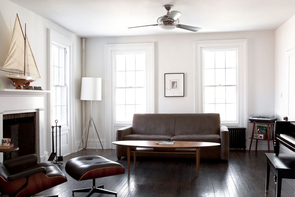Bright, minimalist living room interior with white walls, ceiling fan, and modern furniture arrangement.