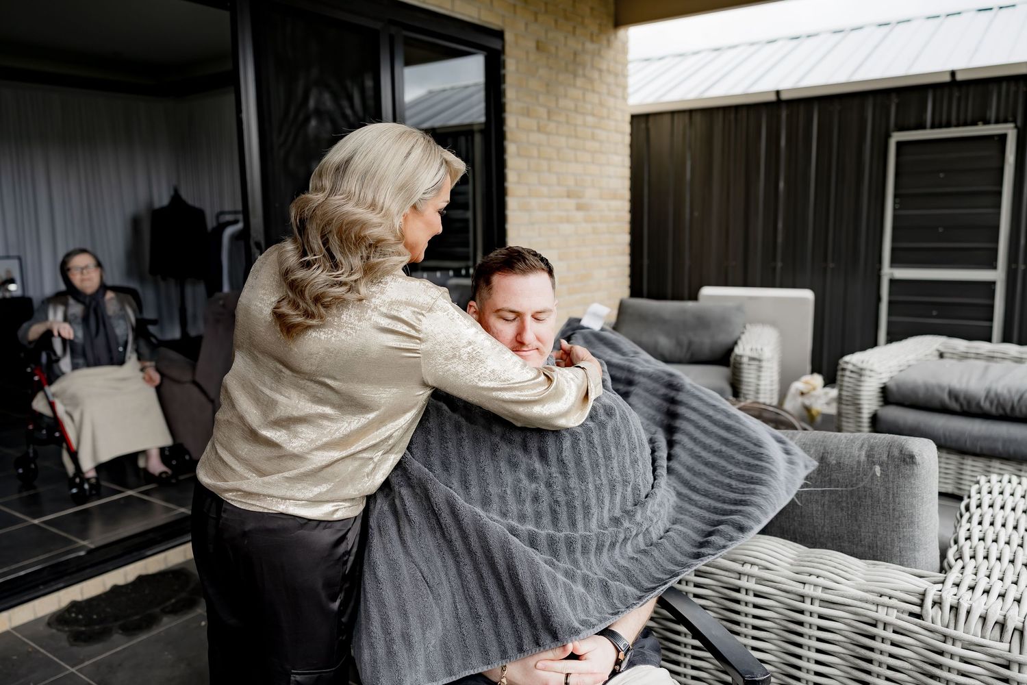 Two people share an emotional embrace while sitting on a gray couch in a living room setting.