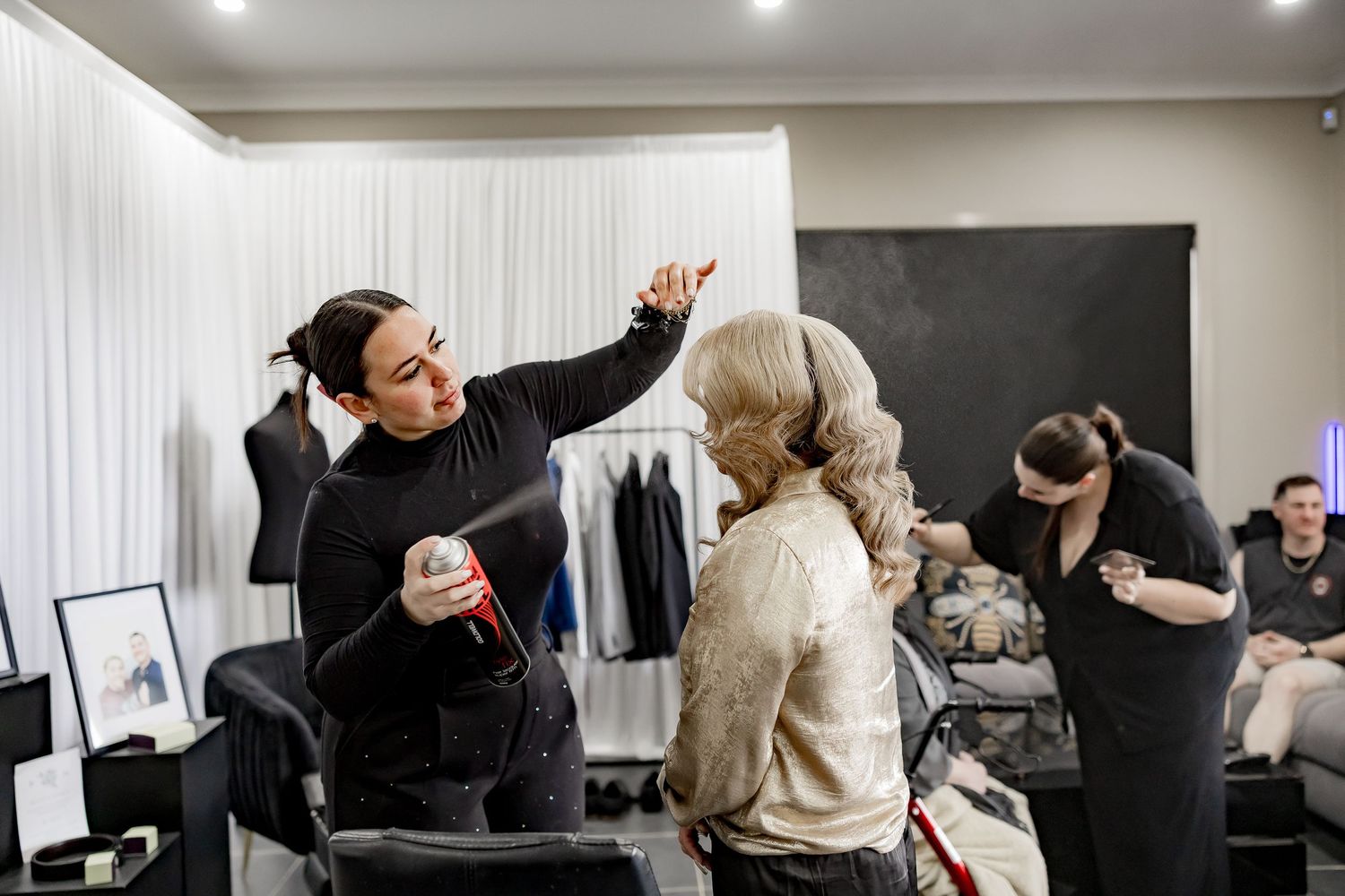 Behind the scenes at a fashion or styling event with people preparing in a bright dressing room area.