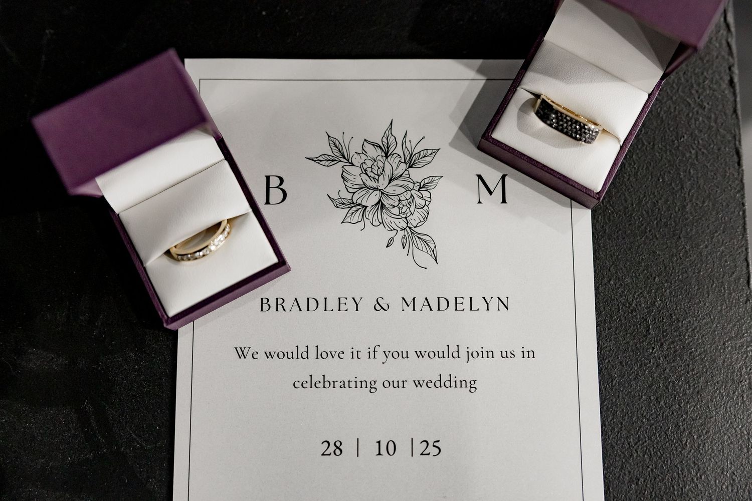Elegant wedding invitation suite featuring plum purple and white cards with floral designs and gold feather accents.