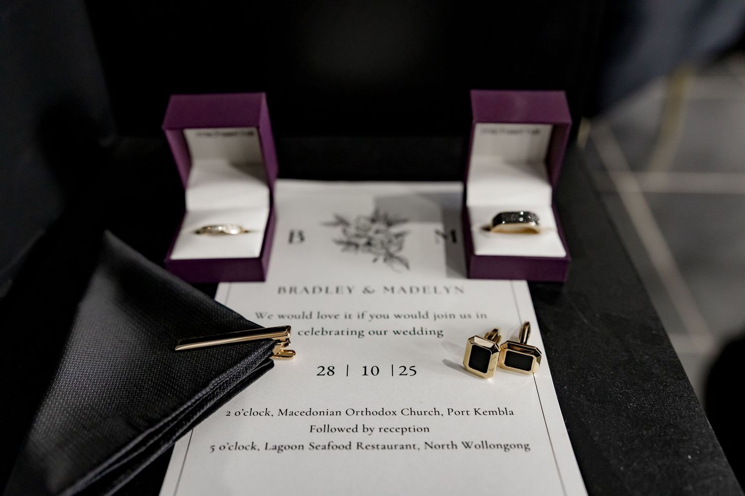 Wedding invitation details and rings displayed on dark surface with elegant purple and white stationery.