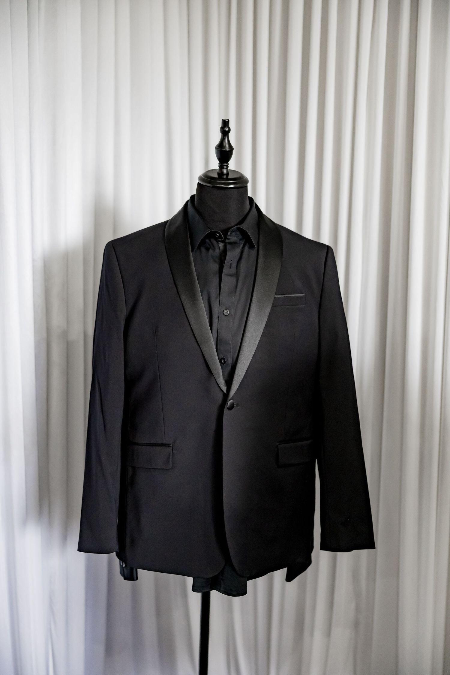 Three black formal suits hanging on display against white curtain.