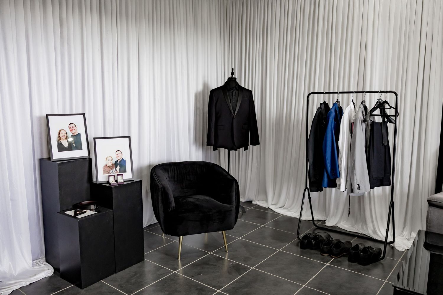 A retail clothing display with black suits and jackets arranged on hangers against a white curtained wall.