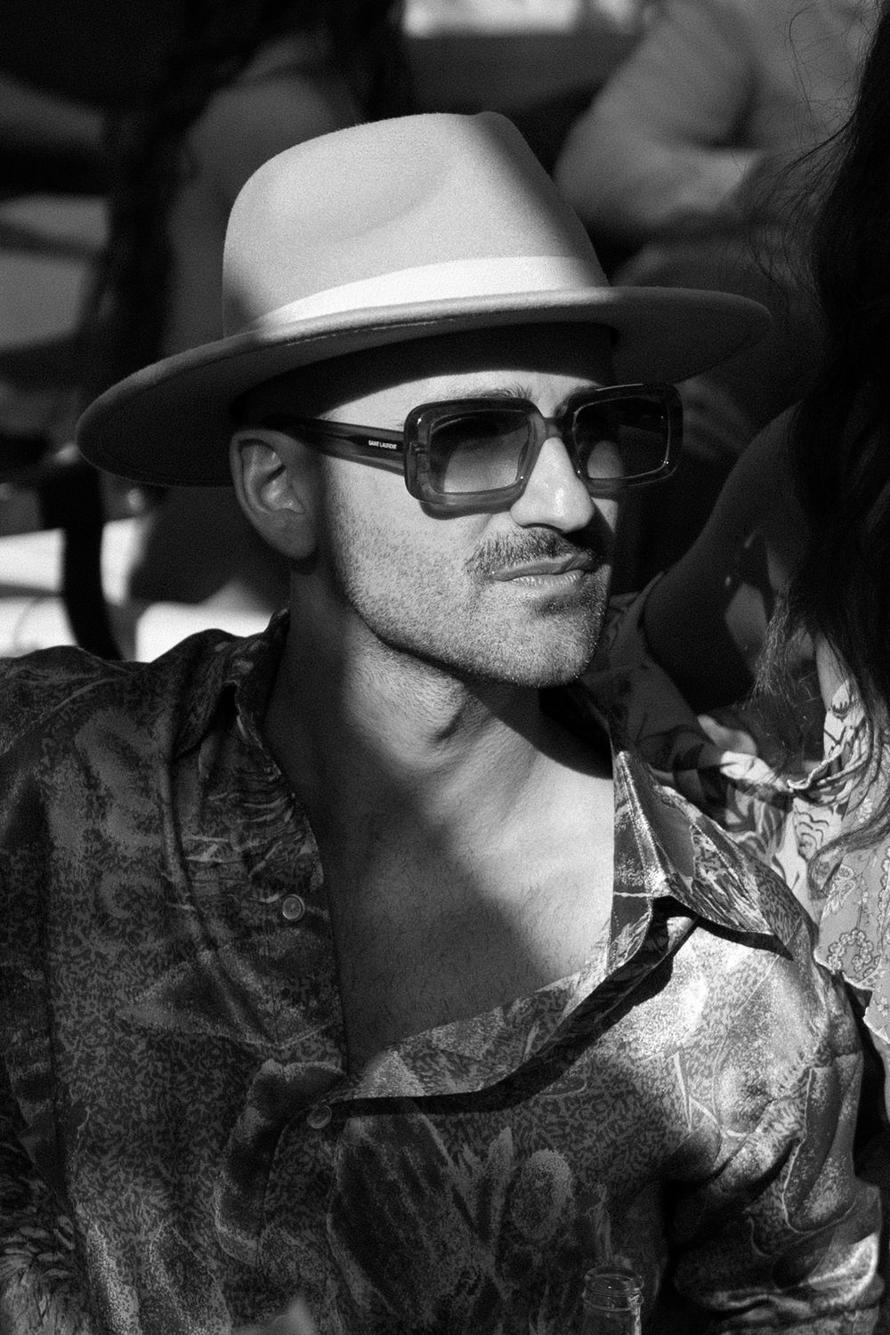 Person wearing sunglasses and white hat in dramatic black and white close-up shot.