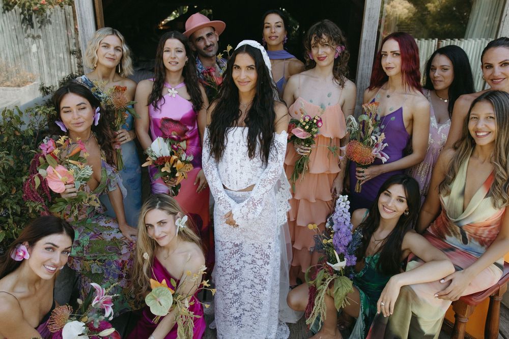 A group of people gather outdoors in formal attire for a wedding celebration with floral decorations.