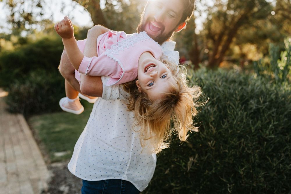 A father playfully holding his child upside down in sunset lighting during an outdoor family photography session in Perth