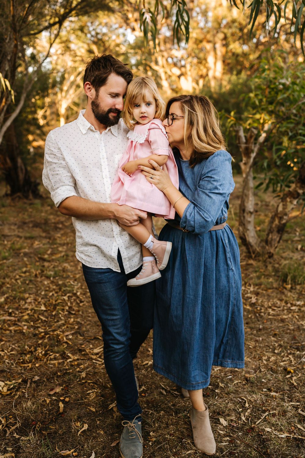 A mother and father walking with their toddler in warm golden sunset lighting during an outdoor family photography session in Perth