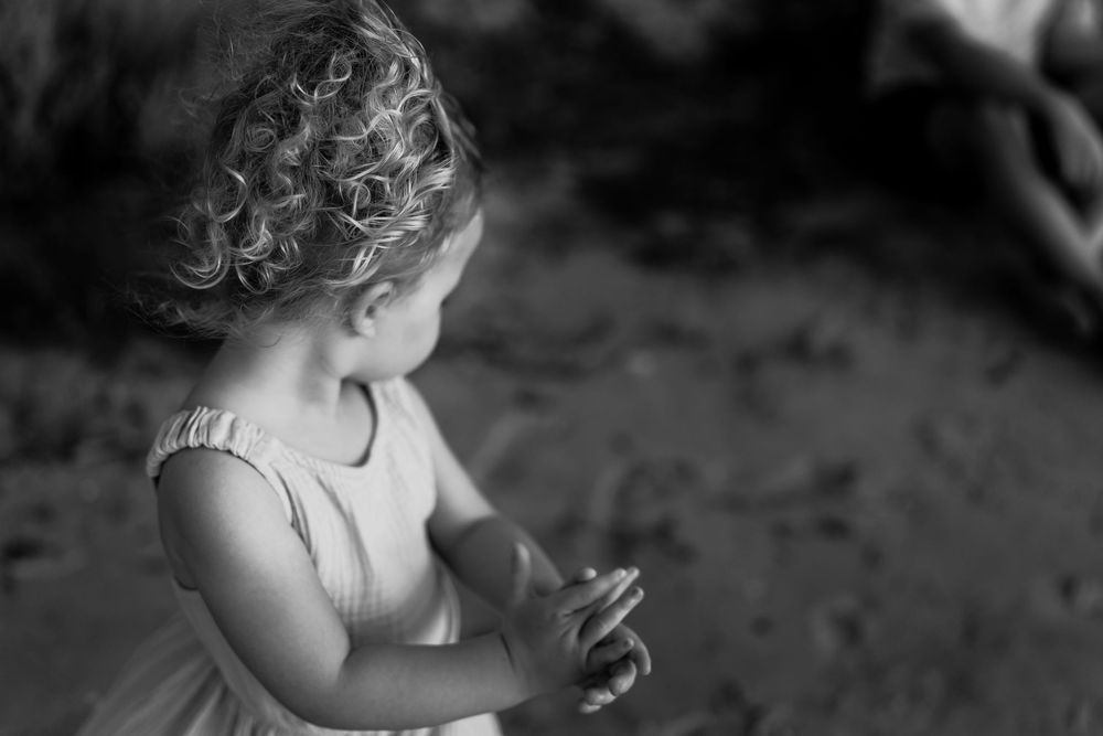 Black and white artistic photograph of a young girl with curly hair playing in the sand at an outdoor sunset photography photoshoot in Perth