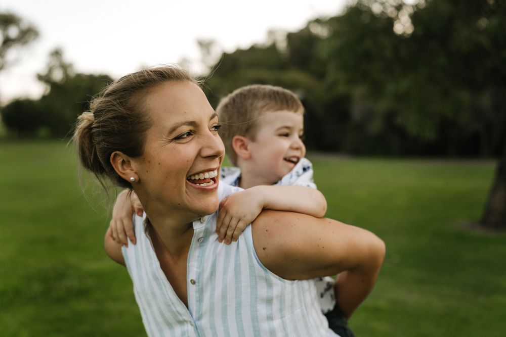 A candid moment of mother with her child on her back during an outdoor Perth family photograph photoshoot.