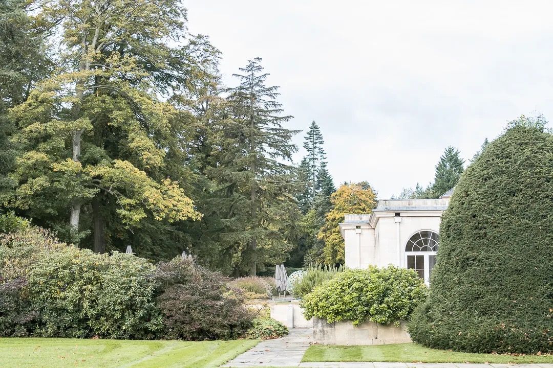 Manicured garden with hedges, trees, and a historic building at the end of the path.