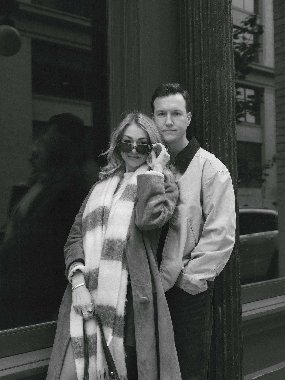 A stylish black and white photo of a couple in winter coats posing together on a city street.