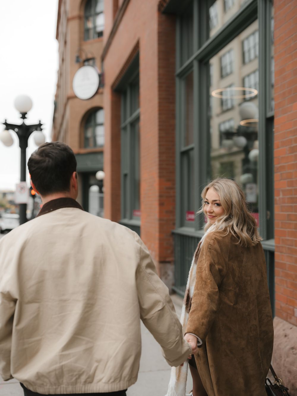 A couple walks together on a city sidewalk wearing stylish winter coats on an overcast day.