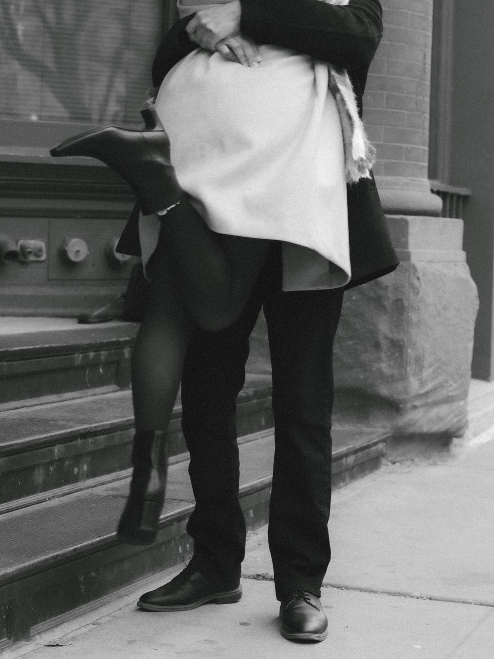 Black and white photo showing legs of two people standing close together on urban steps.