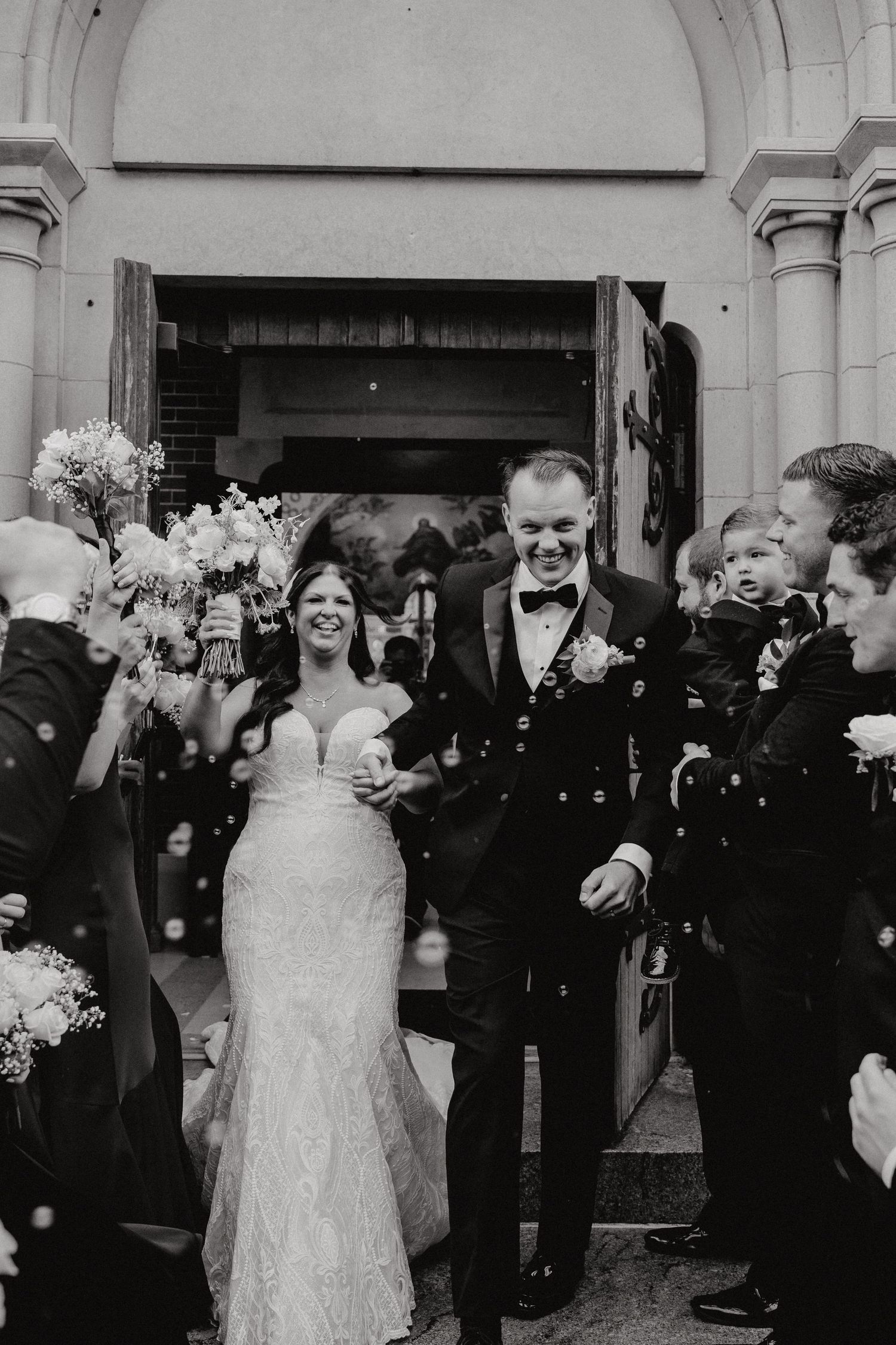 Wedding guests celebrate and wave sparklers outside a venue entrance during a nighttime send-off celebration.