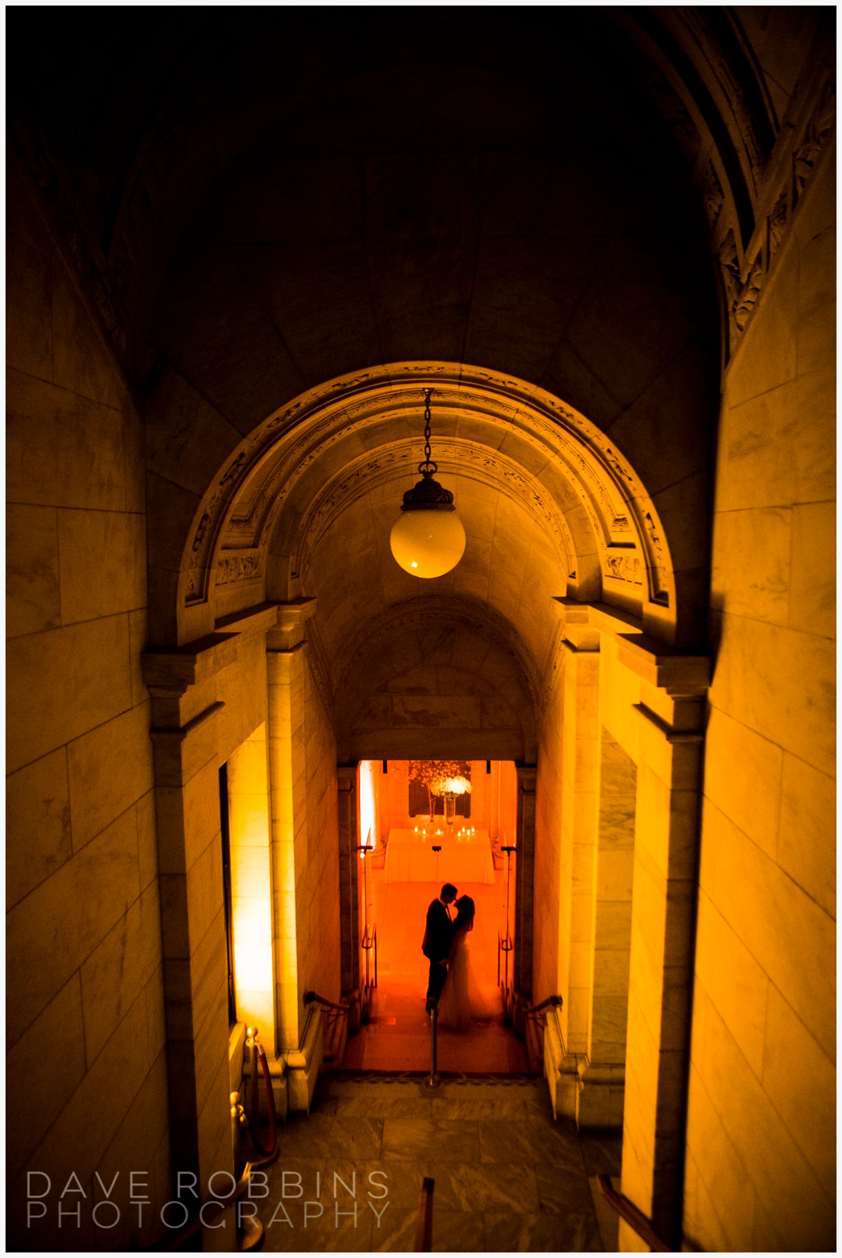 Romantic silhouettes in a warmly lit stone archway corridor creating a dramatic architectural composition.