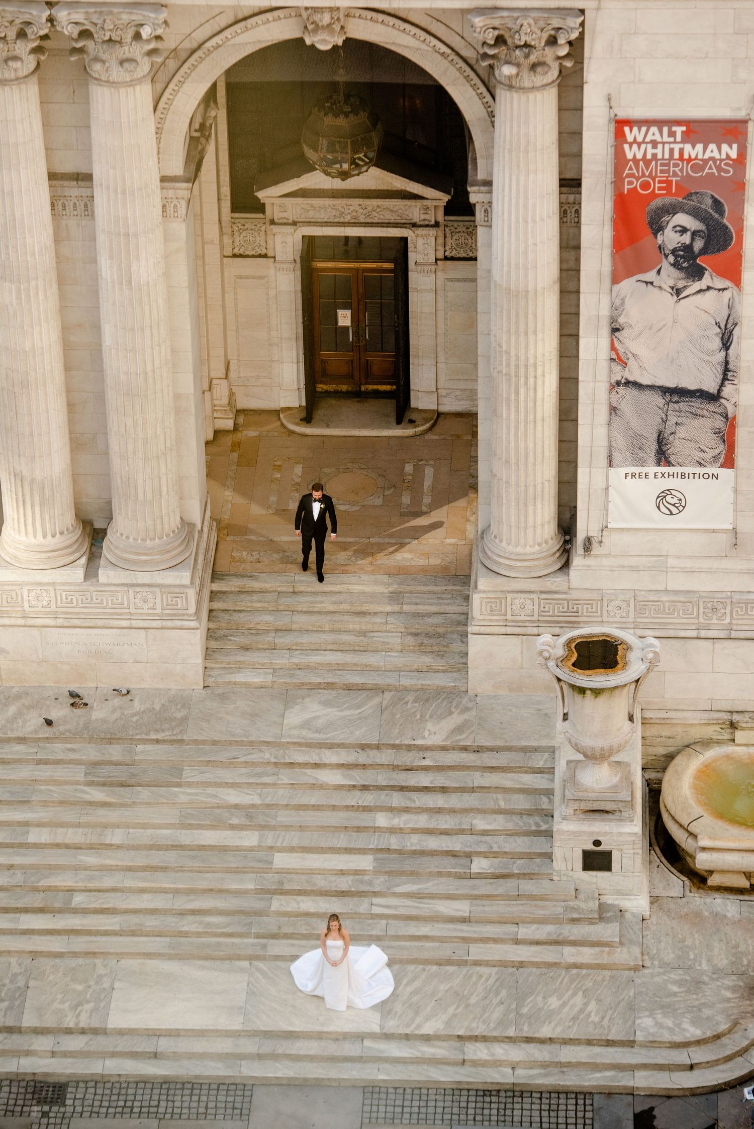 A grand entrance of a classical building with marble columns and steps, featuring a Walt Whitman poster on display.