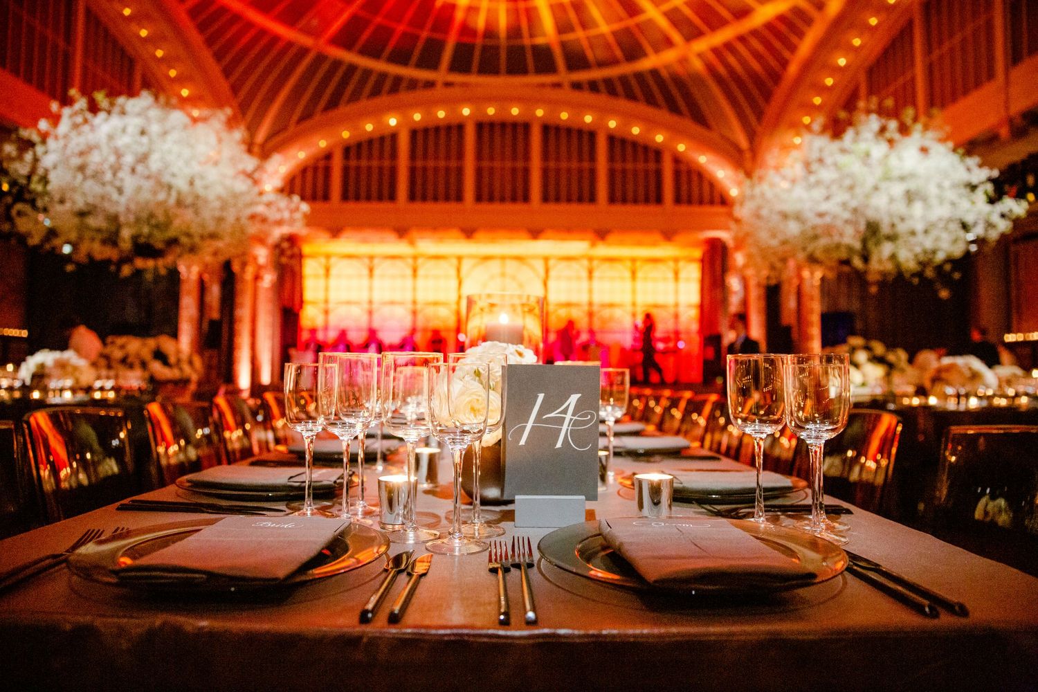 Elegant wedding reception venue with dramatic red uplighting and crystal chandeliers illuminating the space.