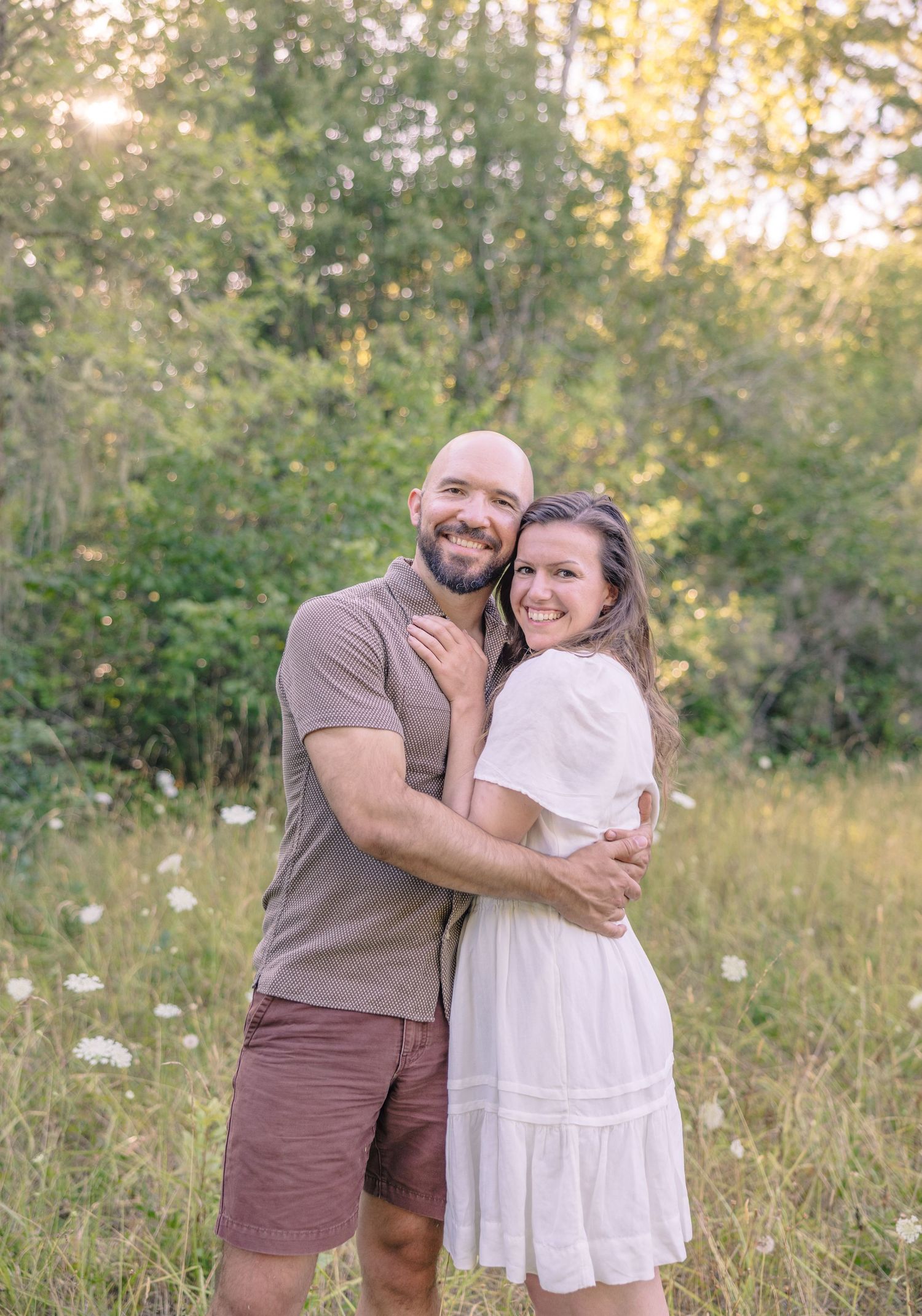 Couple embracing and laughing together in a sunlit meadow with wildflowers.