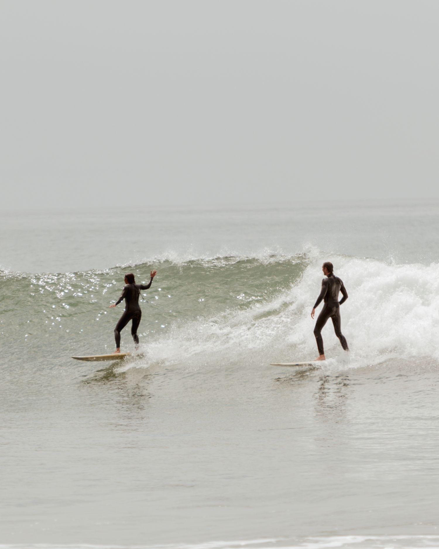 A surfer rides a small wave in choppy ocean conditions on a cloudy day.