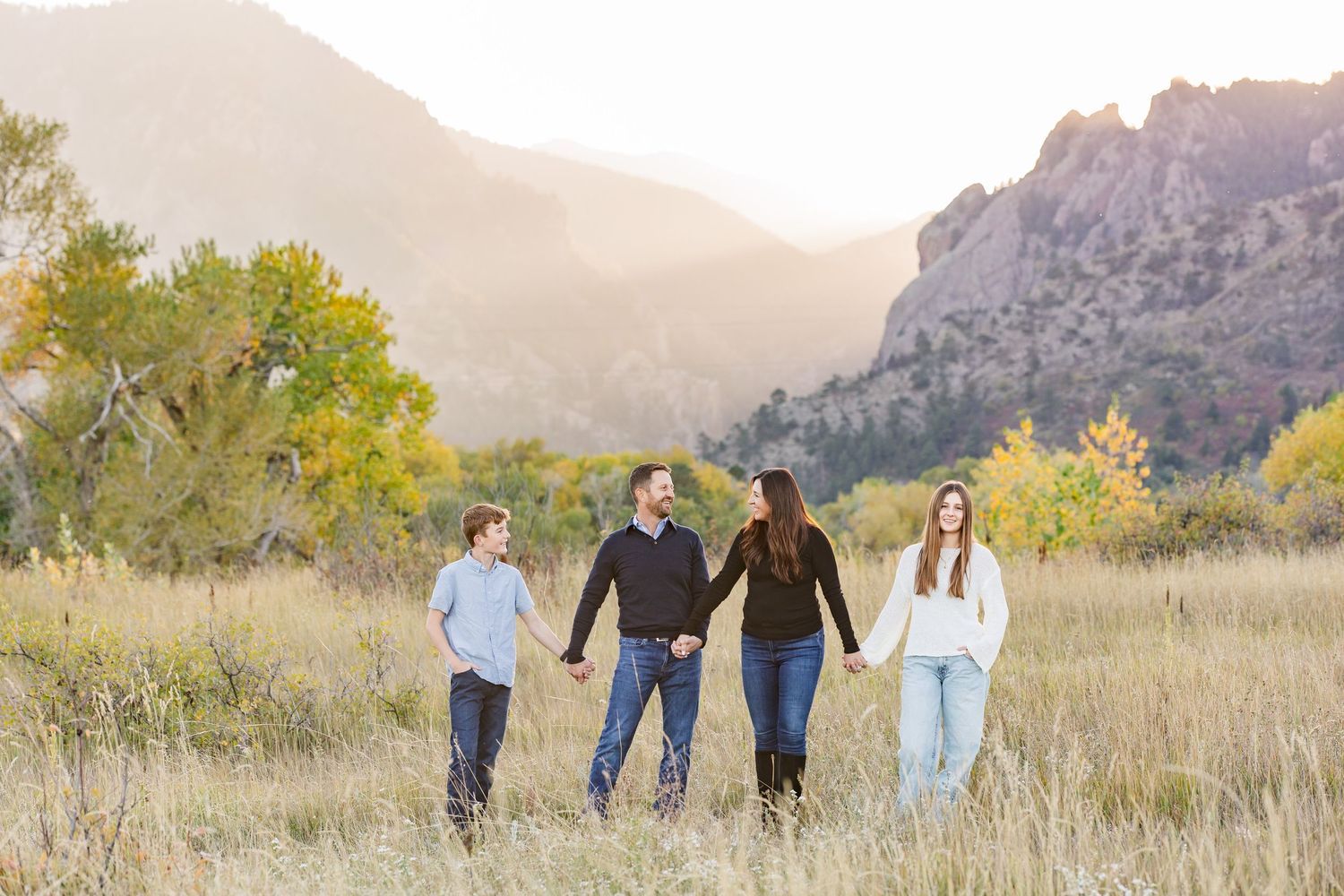 A group walks together through a golden field with autumn trees and mountain cliffs in the background.