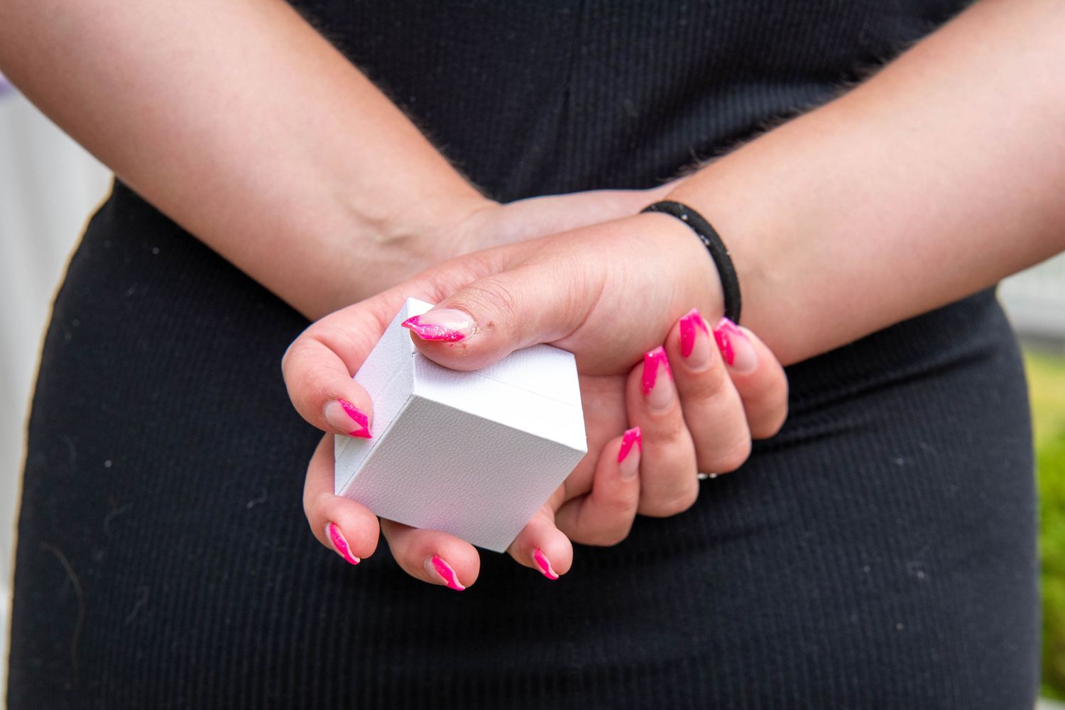 Close-up of hands with pink nail polish holding and examining a white card or paper document.
