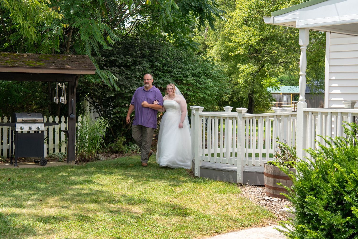 A row of white picket fences lines the perimeter of a lush green yard with trees and shrubs in the background.