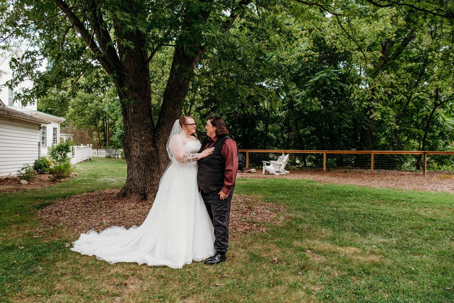 Outdoor wedding photography session with couple and guests on a lush green lawn with mature trees.