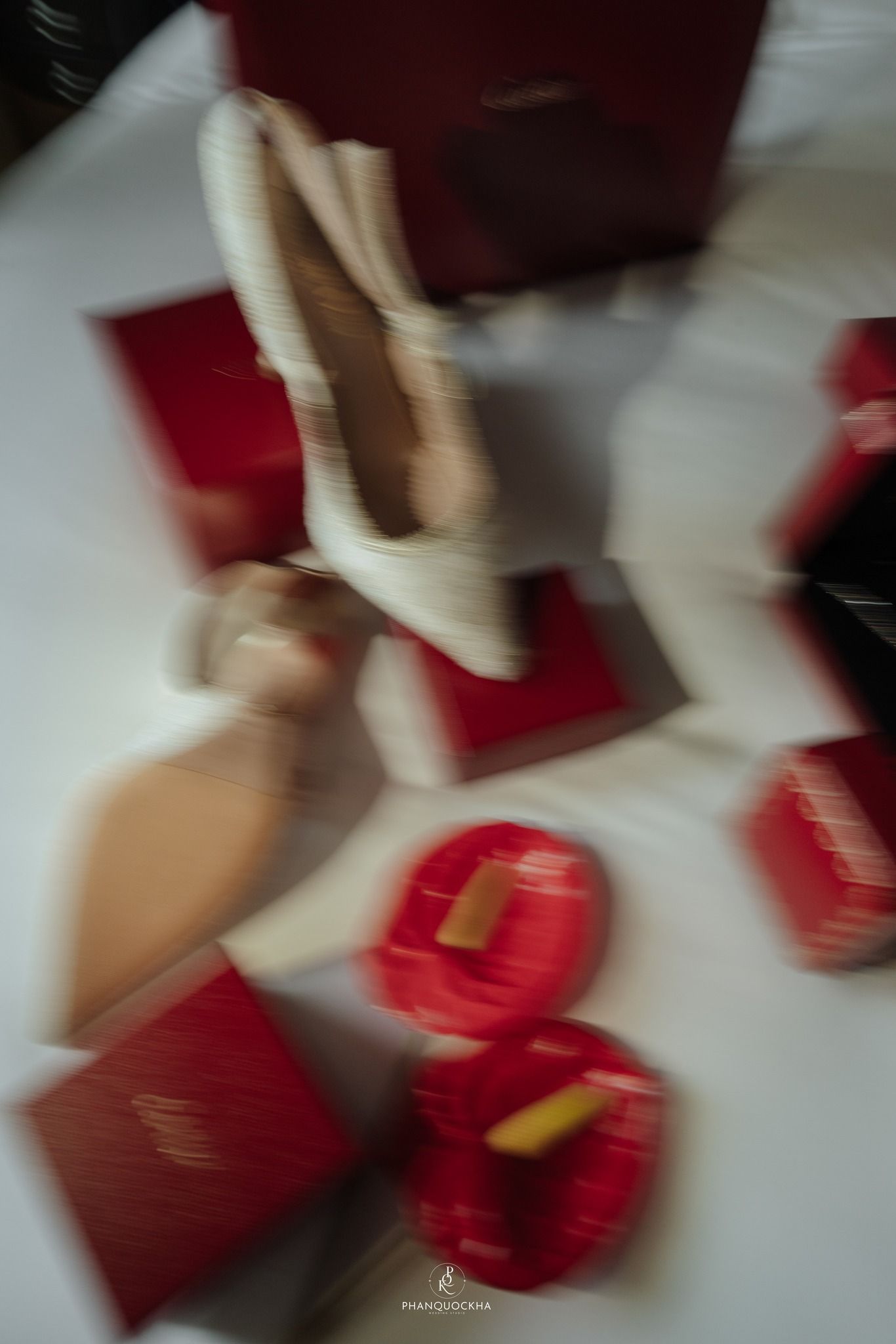 Blurred motion photo of a bride in white surrounded by red gift boxes on white floor.