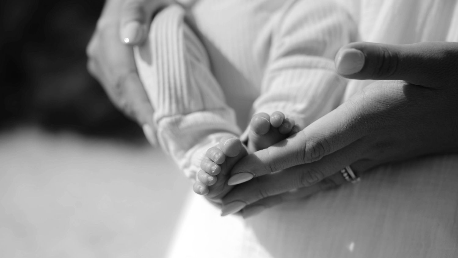 A mother's hands gently cradle her son's feet in a black and white photograph.