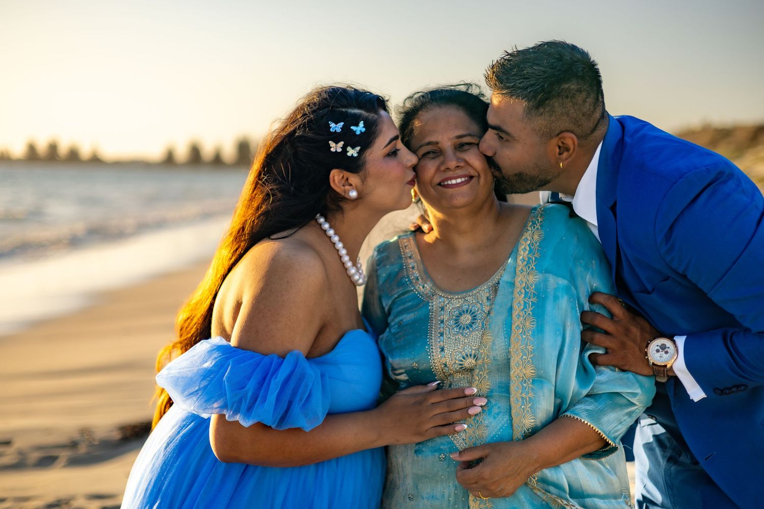 Couple embraces lovingly on a sunny beach at sunset with ocean waves in the background.