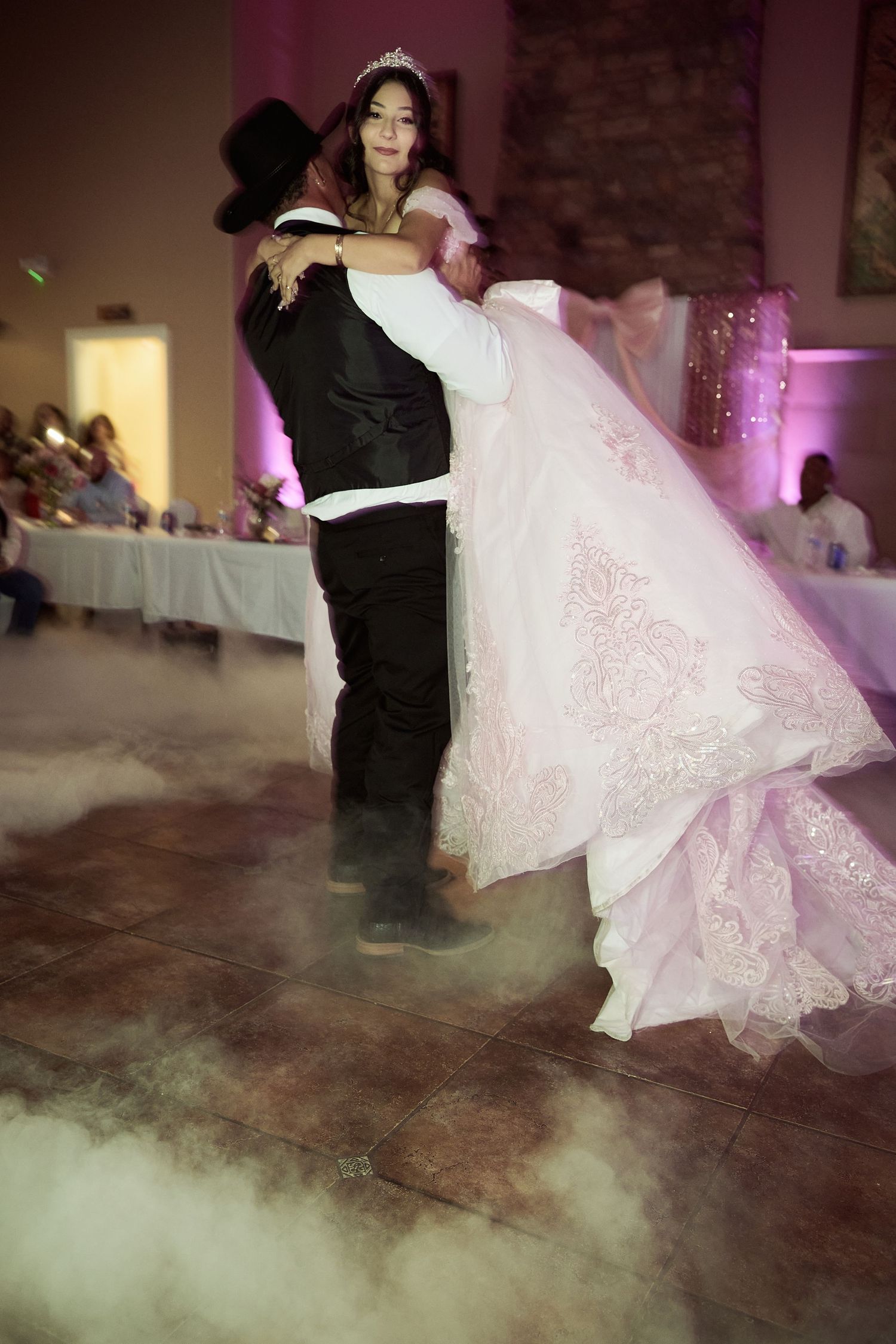 A couple dances their first dance at a wedding reception with fog effects swirling around their feet on the dance floor.