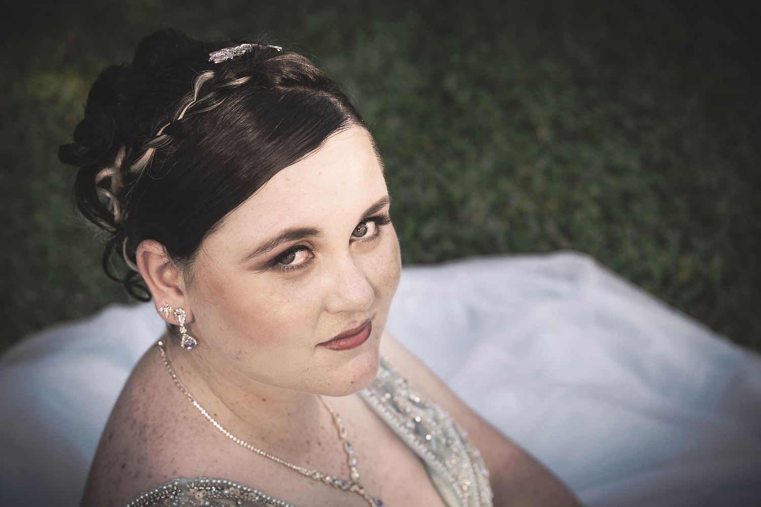 A bride wearing a white wedding gown poses outdoors against a dark background.