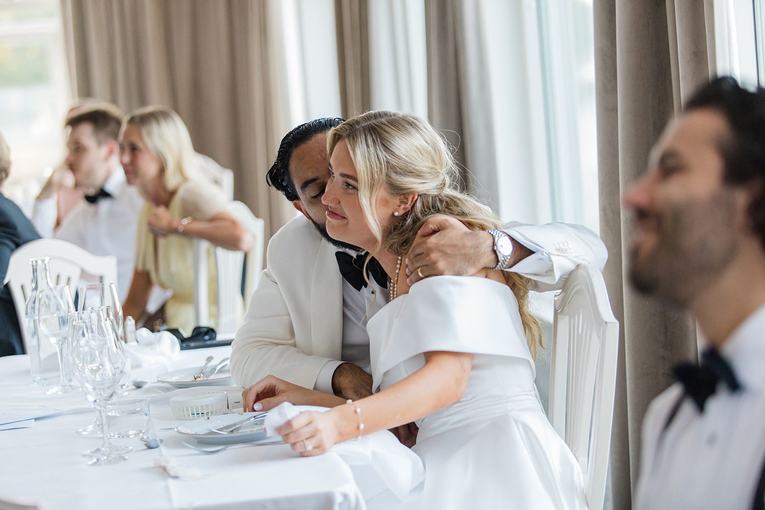 Groomsmen in white dress shirts and black bow ties help each other prepare for a formal wedding event.
