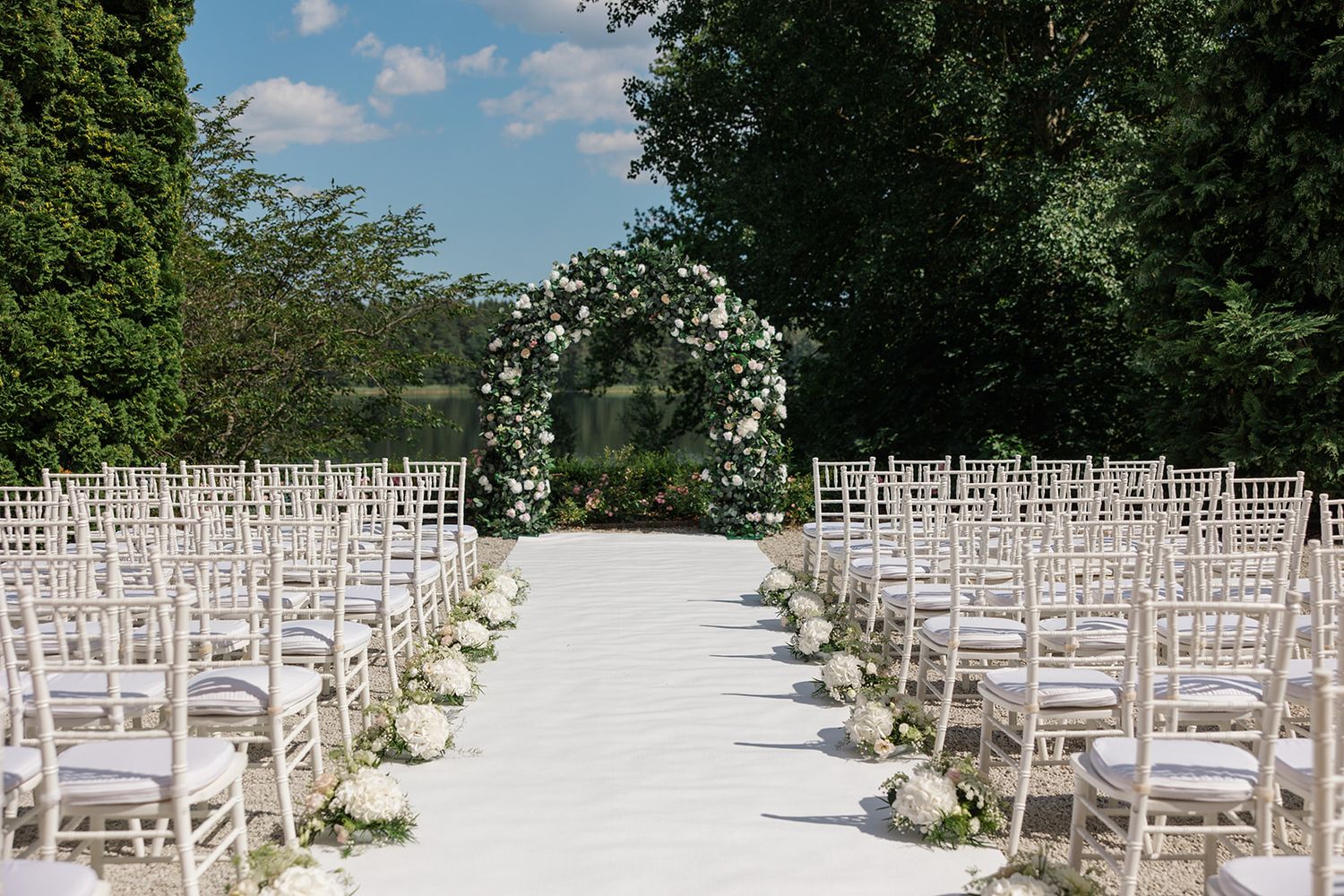 Rows of white wooden chairs set up for an outdoor garden wedding ceremony under a bright blue summer sky.
