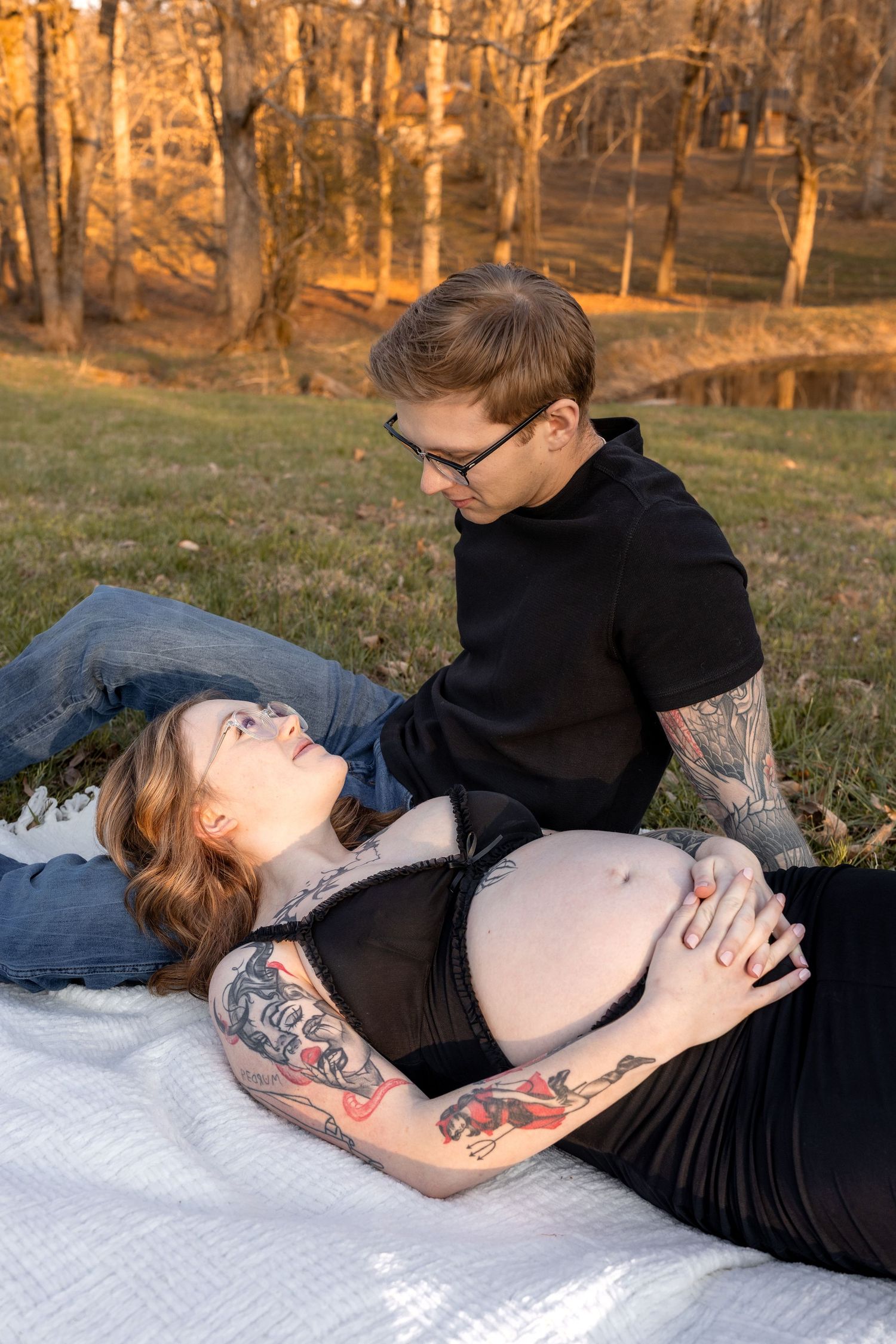 Intimate maternity photoshoot on a blanket during golden hour in a wooded setting.
