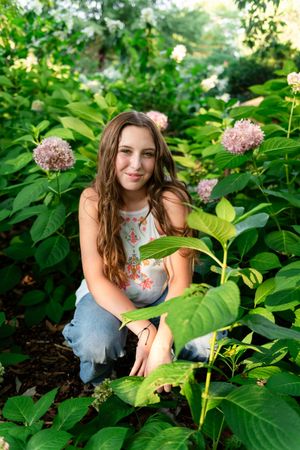 Someone sitting among lush green hydrangea plants in a garden setting.