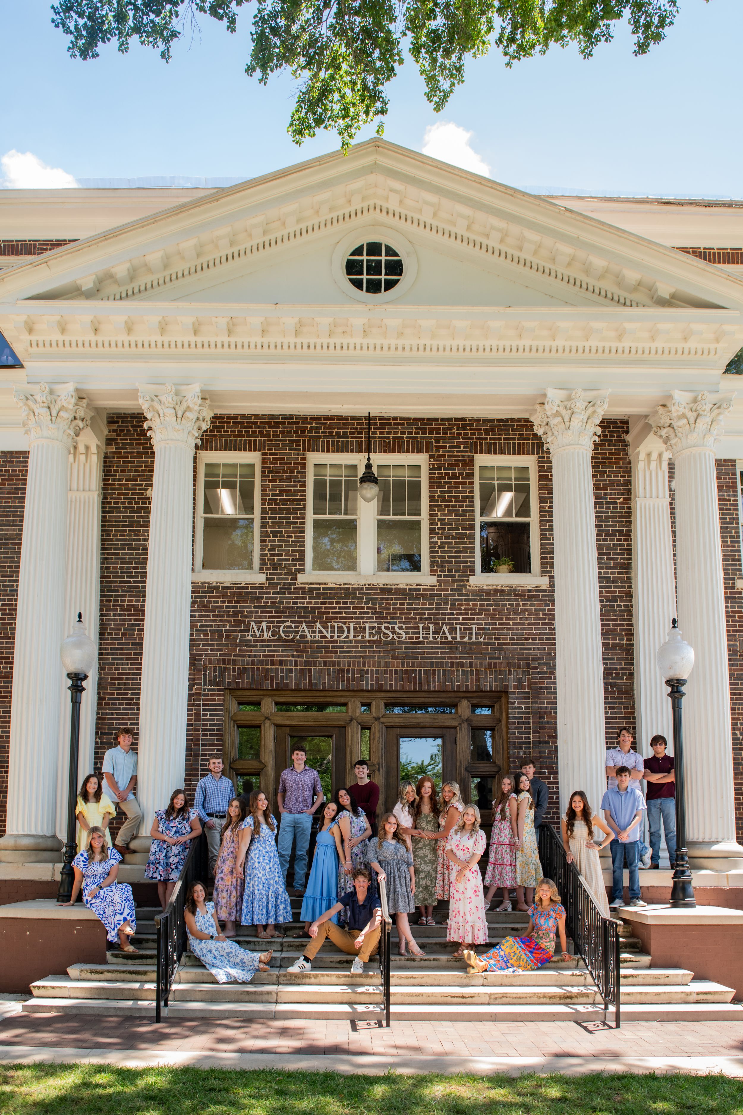 Wide view of McCandless Hall brick building with white columns and waiting crowd.