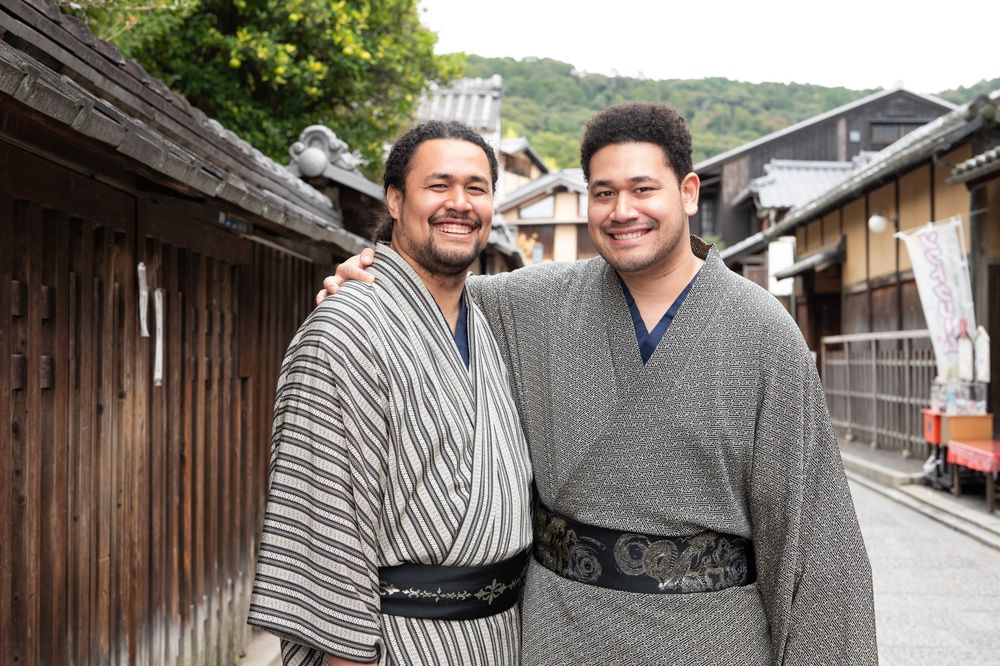 Two men smiling together in traditional Japanese yukata on a historic street.