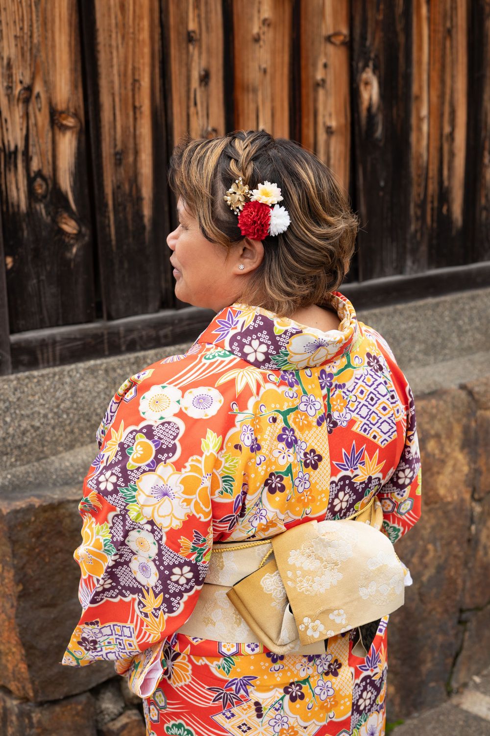 Back view of woman in colorful floral kimono with elegant gold obi and decorative hair flowers.
