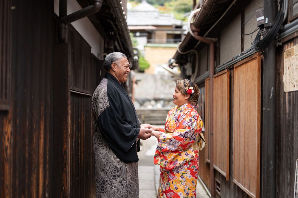 Couple in traditional Japanese kimono share a tender moment in historic Kyoto alleyway.