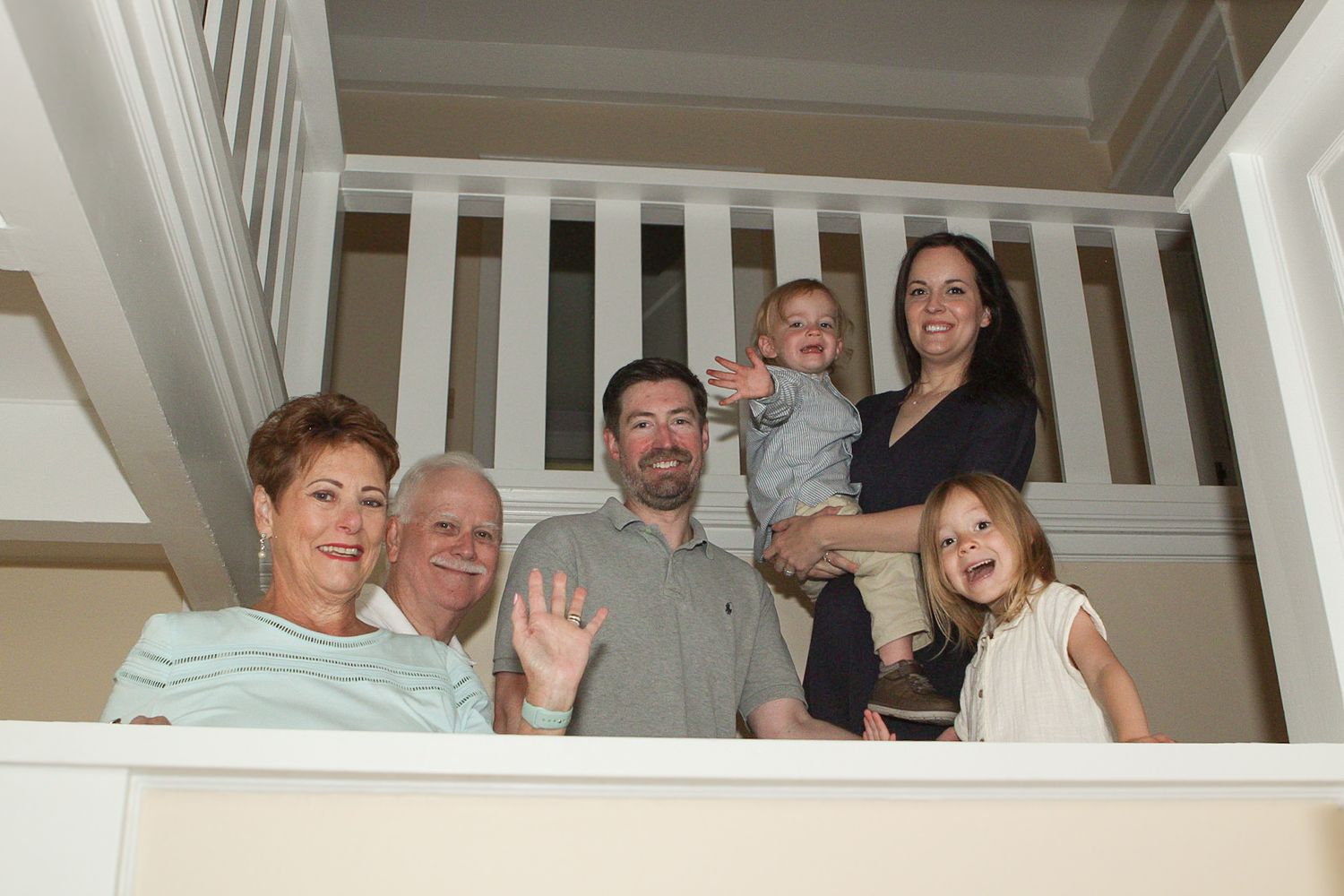 A group poses together on white stairs during an indoor family photo session.