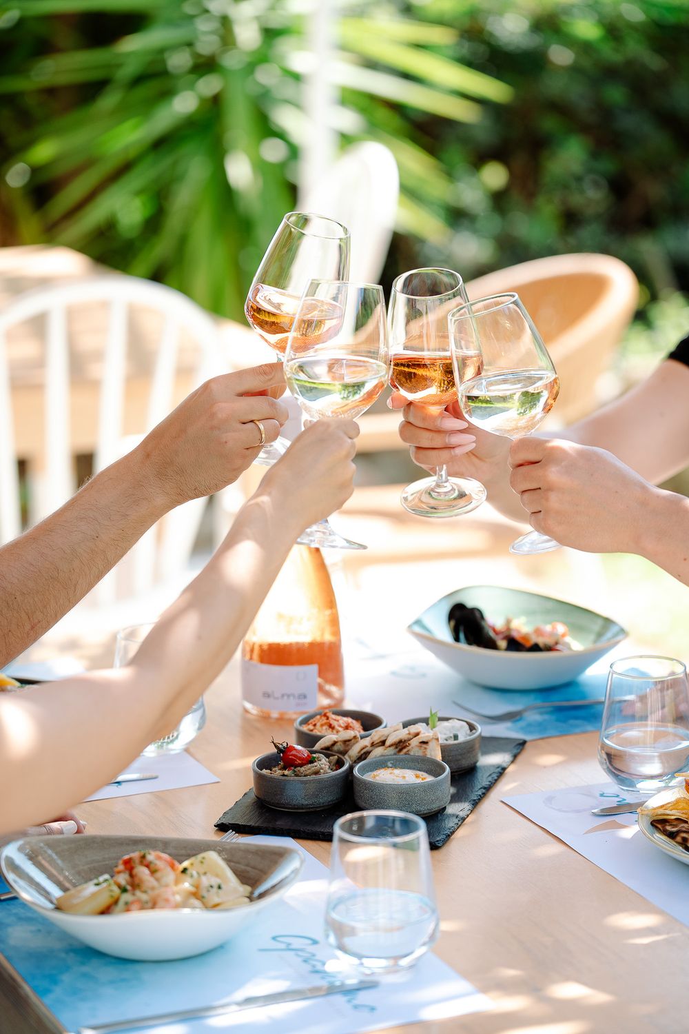 Hands raising glasses over an outdoor lunch table with shared dishes.